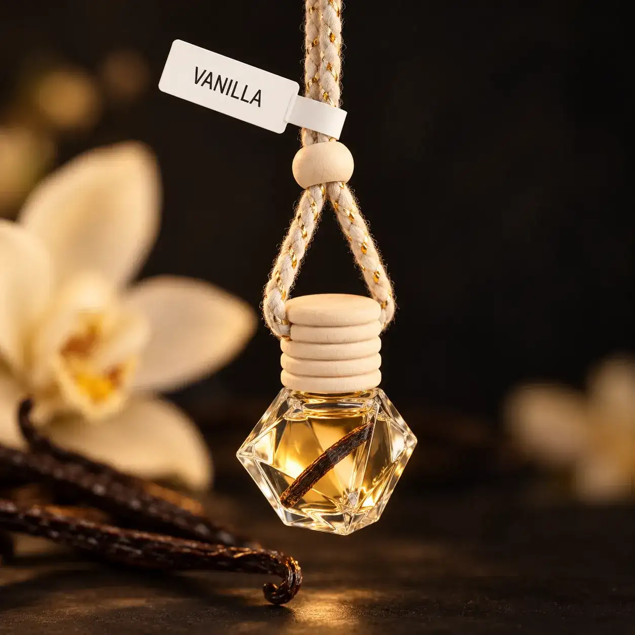 Vanilla car diffuser, a hanging glass bottle with a vanilla bean inside, next to white blossoms