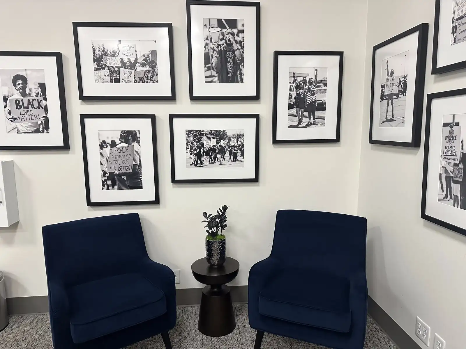 An office lobby with two chairs, a gallery wall and a plant on the side table