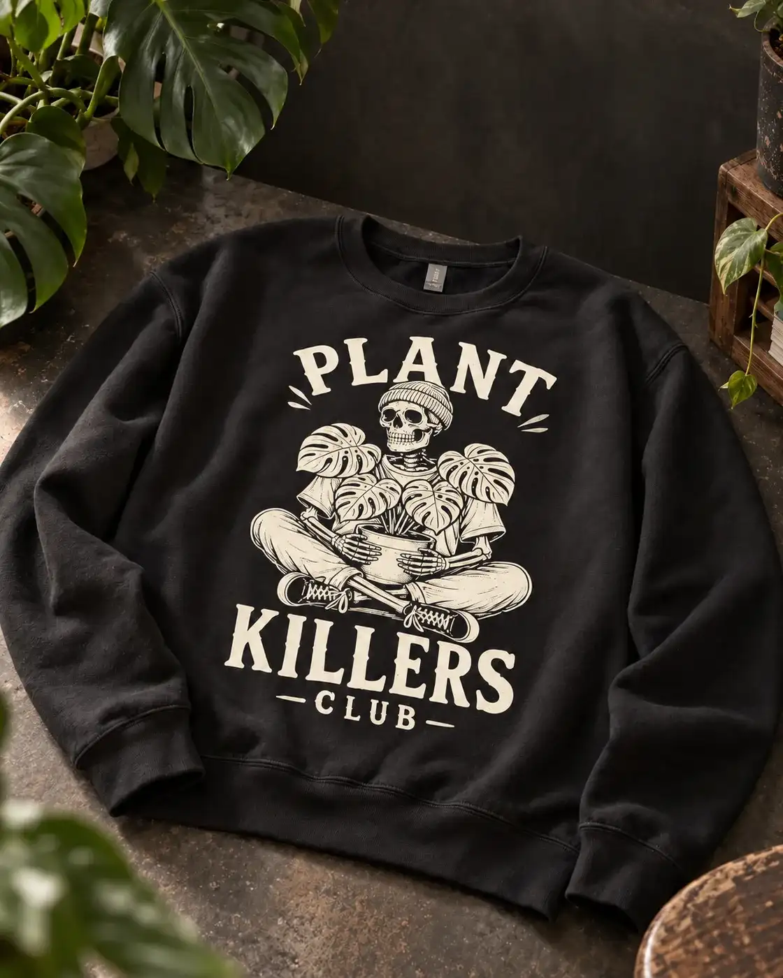 Plant Killers Club crewneck laid flat among potted plants