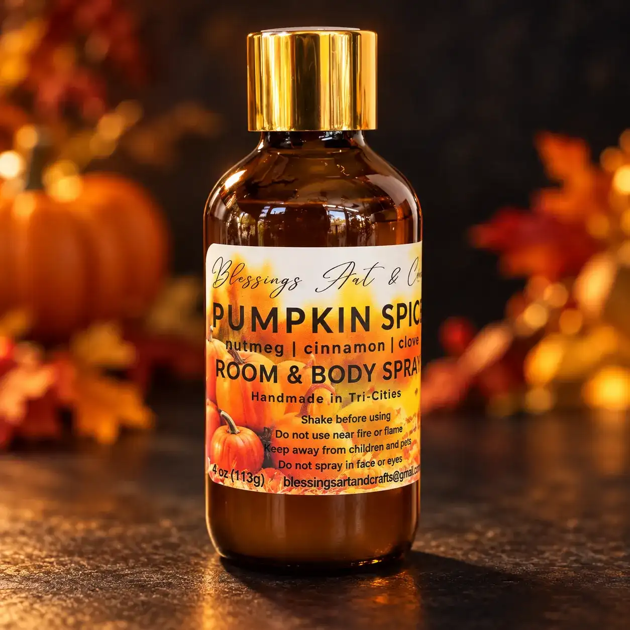 Pumpkin Spice room and body spray in an amber glass bottle with a gold cap, among fall leaves